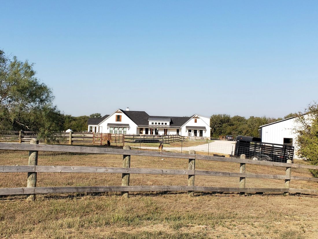 A wide farmhouse-style property with wood fencing under a clear sky, north of Denton