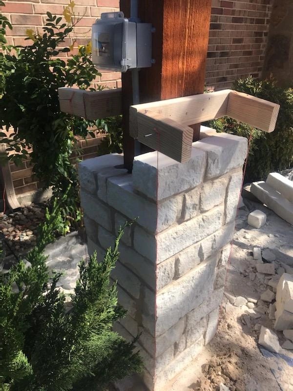 Stacked-stone masonry column being built under a cedar beam