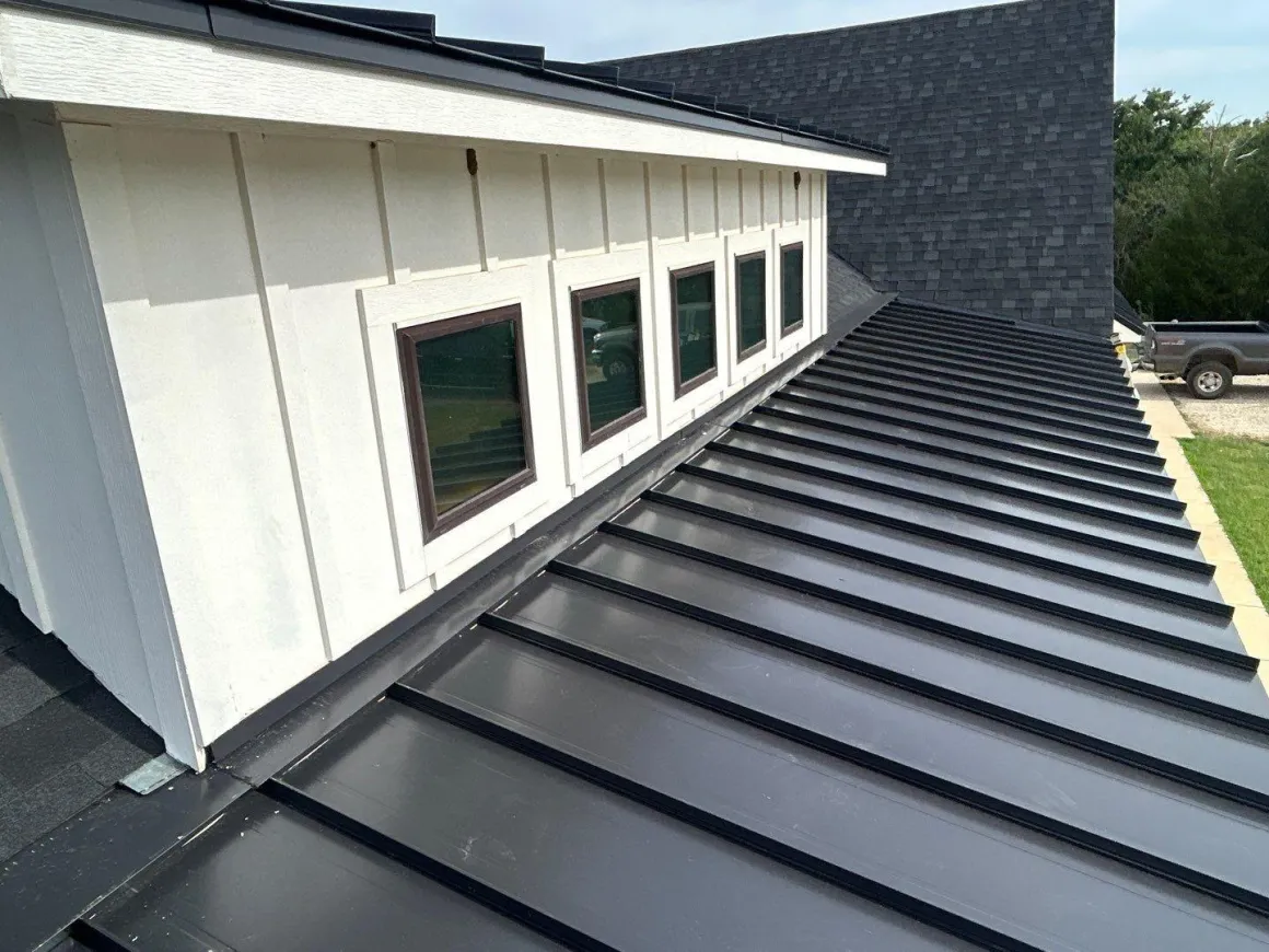 Close-up of a finished standing-seam metal roof running alongside a white board-and-batten dormer, a recent Brick by Brick roofing project