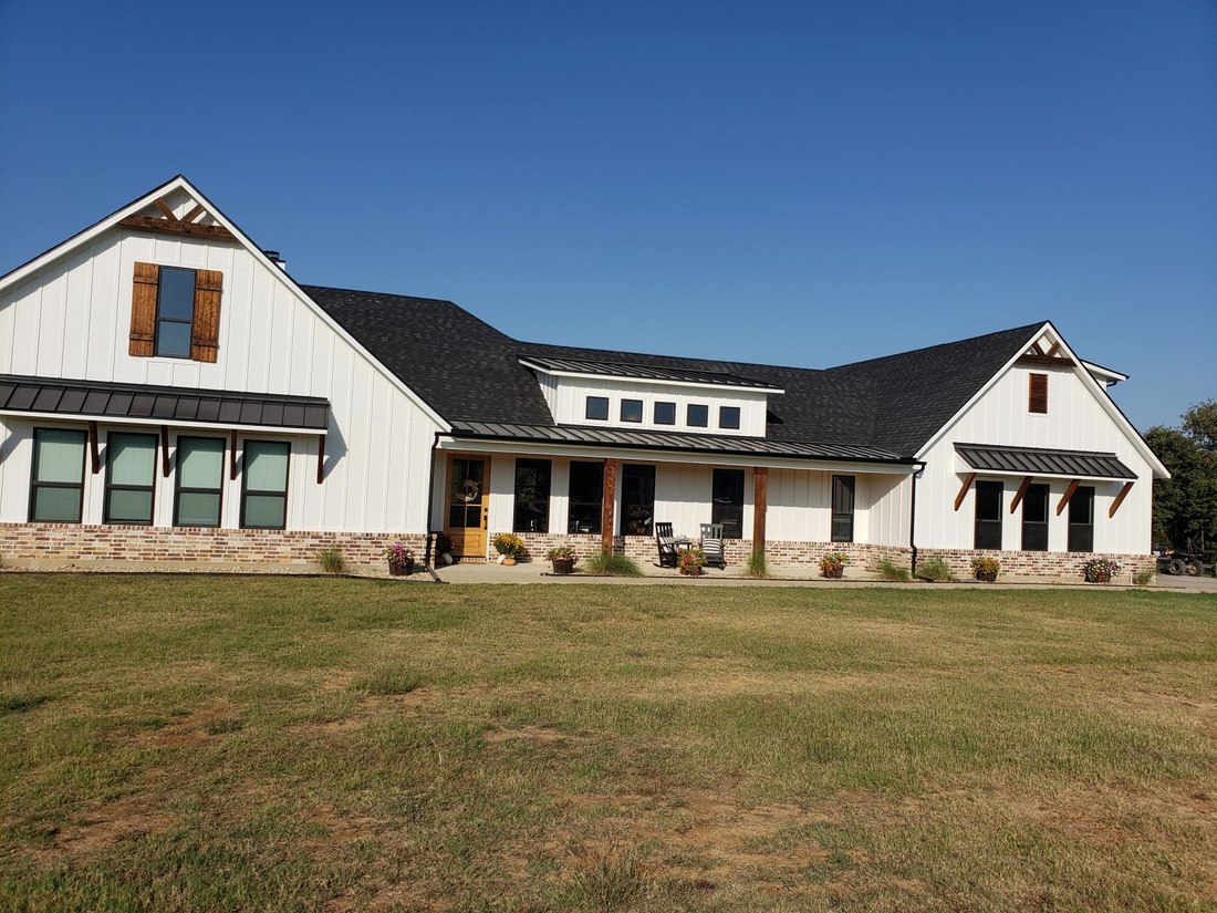 Finished farmhouse-style home with dark asphalt shingle roof and matching standing-seam metal porch roof, a completed Brick by Brick project